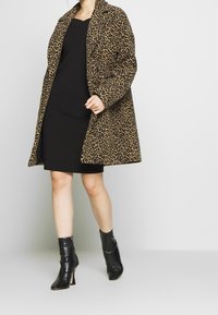 Leopardmönstrad kappa med avslappnad passform, knäppning och bred krage. Bärs över en svart klänning och kombineras med svarta, krokodilprickiga ankelstövlar.