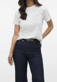 T-shirt bianca in cotone con scollo rotondo abbinata a jeans a vita alta di colore blu scuro; cintura nera con fibbia ovale dorata e dettagli di cucitura.