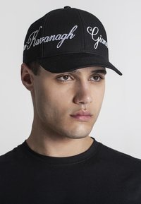 Svart basebollkeps med vitt broderat text på framsidan. Designen har en strukturerad krona och en böjd skärm.
