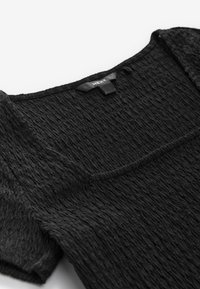 Must tekstuurne pluus ruudukujulise kaelusega, millel on peened kortsudetailid ja lühikesed varrukad. Kangas paistab pehme ja kerge.