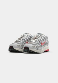 Nike-Sneaker mit einem grauen Mesh-Obermaterial, roten Akzenten, strukturierten Überzügen, einer gepolsterten Sohle und einer schwarzen Gummisohle.