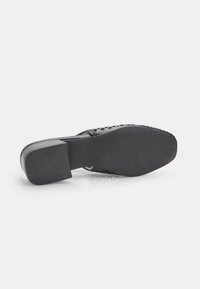 Zapato negro de tacón con diseño perforado, punta cuadrada y tacón bajo de bloque. La suela presenta un acabado texturizado de goma para mayor agarre.