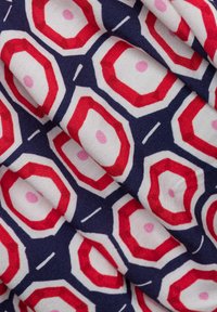 Tessuto decorato con forme ottagonali rosse e rosa su uno sfondo blu navy, con accenti bianchi e texture visibile.