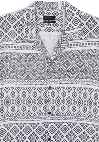 Chemise à motifs noir et blanc avec une coupe décontractée, présentant des designs géométriques, un col et une fermeture à boutons à l'avant. En coton.