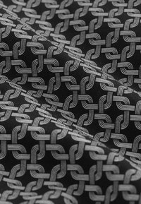 Tessuto nero con un motivo geometrico di linee argentate intrecciate che creano un disegno ripetitivo e strutturato. Texture morbida con una lucentezza.