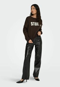 Bruine sweatshirt met "STUDY" in witte letters, gecombineerd met hoge zwarte nepleren broeken en zwarte hakken.