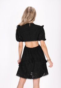 Rochie neagră cu un model texturat, mâneci bufante, decupaj la spate, fustă cu volane și tiv decorativ cu ondulații.