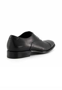 Black leather dress shoe with a rounded toe, smooth texture, lacing detail, and a low stacked heel. Side view shows minimal design elements.