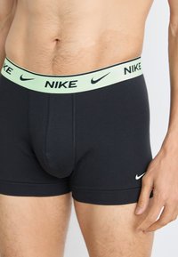 Schwarze Baumwoll-Boxershorts mit einem hellgrünen Nike-Logo-Bund und kleinem weißen Nike-Swoosh auf der Vorderseite. Weicher Stoff, körpernahe Passform.