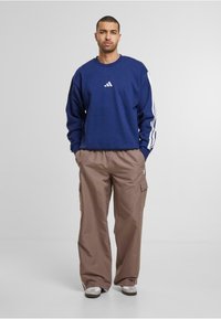 Marinblå sweatshirt med vitt logotyp, tillsammans med beige cargobyxor med sidofickor och elastisk midja. Bärs med ljusa sneakers.