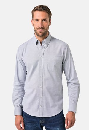 Chemise boutonnière gris clair avec une poche, à manches longues et col pointu, en tissu lisse. Portée avec un jean bleu.