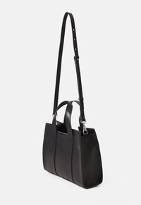 Sac à main en cuir noir texturé avec deux petites poignées et une longue bandoulière réglable, présenté sur fond blanc.