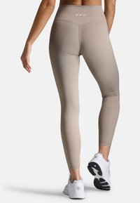 Beige high-waisted Leggings mit elastischem Bund, glatter Textur und seitlichen Nähten, kombiniert mit weißen Sportschuhen.