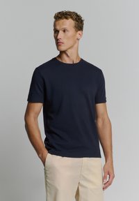 Navyblauwe t-shirt met korte mouwen van textuurstof, ronde hals en een aansluitend ontwerp, gecombineerd met lichtgekleurde broeken.