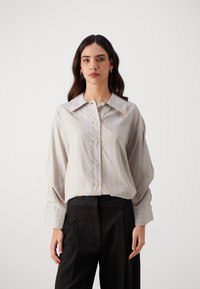 Cămașă dungi albastre și crem dintr-un material neted, cu guler clasic, butoni pe față și mâneci lungi. Asortată cu pantaloni negri.