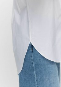 Weißes Hemd mit gekurvtem Saum, aus glattem Stoff, kombiniert mit hellblauen Jeans aus Denim mit Knopfverschluss.