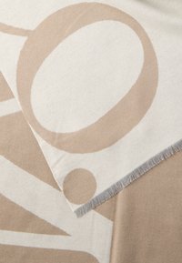 Material textil cu model geometric bej și crem, cu marginile tocite, prezentând forme abstracte mari și o textură netedă.