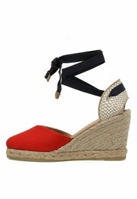 Espadrille à talon compensé en toile rouge avec une semelle en jute tissé, des liens noirs autour de la cheville et un accent arrière clair à motifs. Design à bout arrondi.