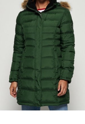 Femme portant un long manteau d'hiver matelassé vert foncé avec une capuche bordée de fourrure marron et une fermeture éclair à l'avant.