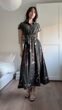 Grønn blomsterkjole med korte ermer, knappet krage og knyttet midje. Har rosa blomster på et flytende stoff. Svarte sandaler med stropper.