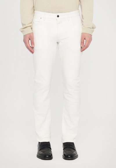Jean en denim blanc avec une coupe slim, design à cinq poches et un bouton noir à la taille, associé à des chaussures noires. Texture lisse.