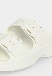 Λευκό σανδάλι με δύο ρυθμιζόμενες αγκράφες και υφασμένο πάτο, κατασκευασμένο από ελαφρύ χυτευμένο υλικό.