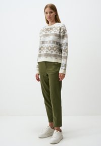 Maglione a maglia con un motivo geometrico in crema, beige e blu, abbinato a pantaloni aderenti verde oliva e sneakers bianche.