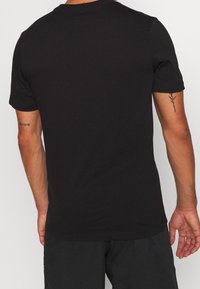 Camiseta negra de manga corta hecha de tela suave, con cuello redondo estándar, textura lisa y diseño minimalista sin gráficos visibles.
