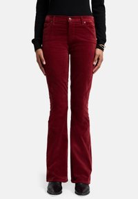 Rode corduroy broek met uitlopende pijpen, voorzien van een soepele textuur, vijf zakken en een metalen knoopsluiting. Gemaakt in combinatie met een zwarte top en zwarte schoenen.