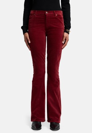 Rode corduroy broek met uitlopende pijpen, voorzien van een soepele textuur, vijf zakken en een metalen knoopsluiting. Gemaakt in combinatie met een zwarte top en zwarte schoenen.