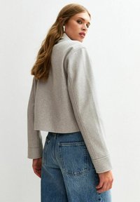 Korte grijze jas met lange mouwen, gemaakt van zacht materiaal, met een minimalistisch ontwerp, gecombineerd met hoge taille blauwe jeans.