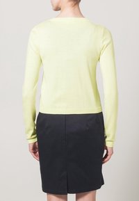 Helles gelbes, eng anliegendes Sweatshirt mit langen Ärmeln, geripptem Ausschnitt und Bündchen, kombiniert mit einem dunklen Rock. Weiche Textur, verkürzte Länge.