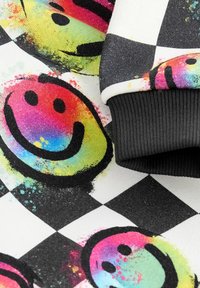 Tissu à carreaux noir et blanc avec des visages souriants peints aux couleurs de l'arc-en-ciel et un bord-côte noir d'un vêtement.
