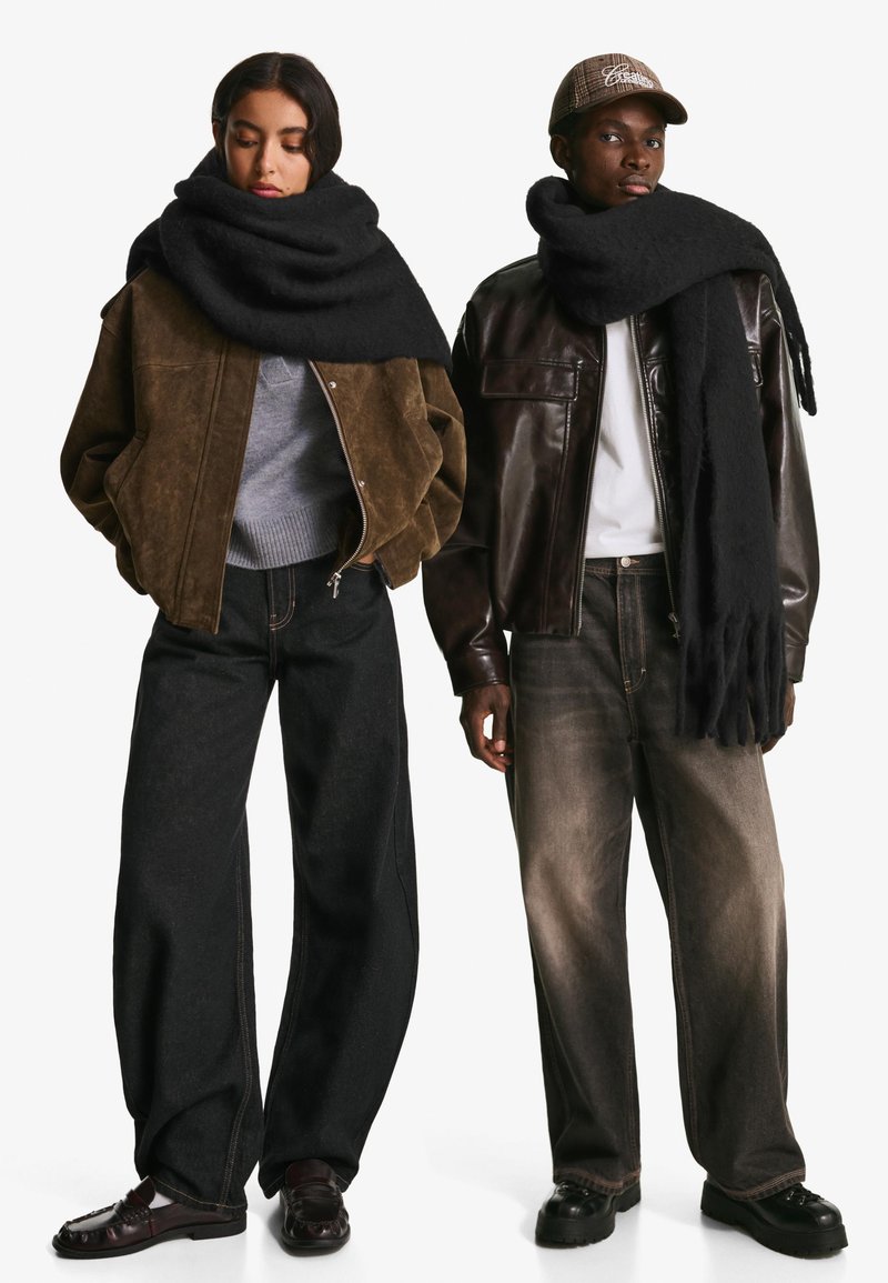 Rjava zamšasta jakna, siva pulover, črn šal na ženski. Moški v rjavi usnjeni jakni, beli majici, črnem šalu in temnih kavbojkah.