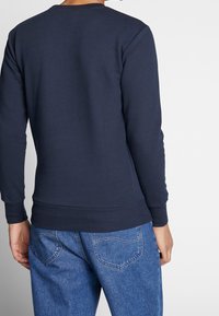 Felpa blu navy con maniche lunghe, polsini e orlo a costine, tessuto morbido, indossata con jeans di denim blu chiaro.