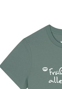 T-shirt en coton vert sauge à manches courtes avec texte imprimé blanc. Tissu légèrement texturé, col rond et couture soignée le long des bords.