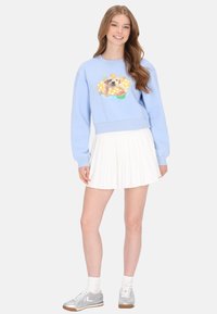Világoskék pulóver vidám kutyás grafikával, pöttyökkel és virágos díszítéssel, hozzá fehér, pliszírozott szoknya és ezüst tornacipők.