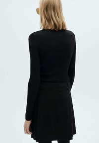 Top noir à manches longues côtelé associé à une jupe évasée noire. La tenue présente une silhouette ajustée et une texture lisse.