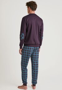 Maglione a maniche lunghe di colore viola con toppe blu a fantasia sui gomiti, abbinato a pantaloni a quadri blu e neri, con orli risvoltati e una vestibilità comoda.