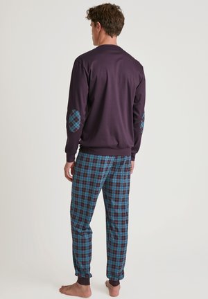 Haut à manches longues violet avec des patchs de coudes bleus à motifs, associé à un pantalon à carreaux bleu et noir, comprenant des ourlets retroussés et une coupe décontractée.