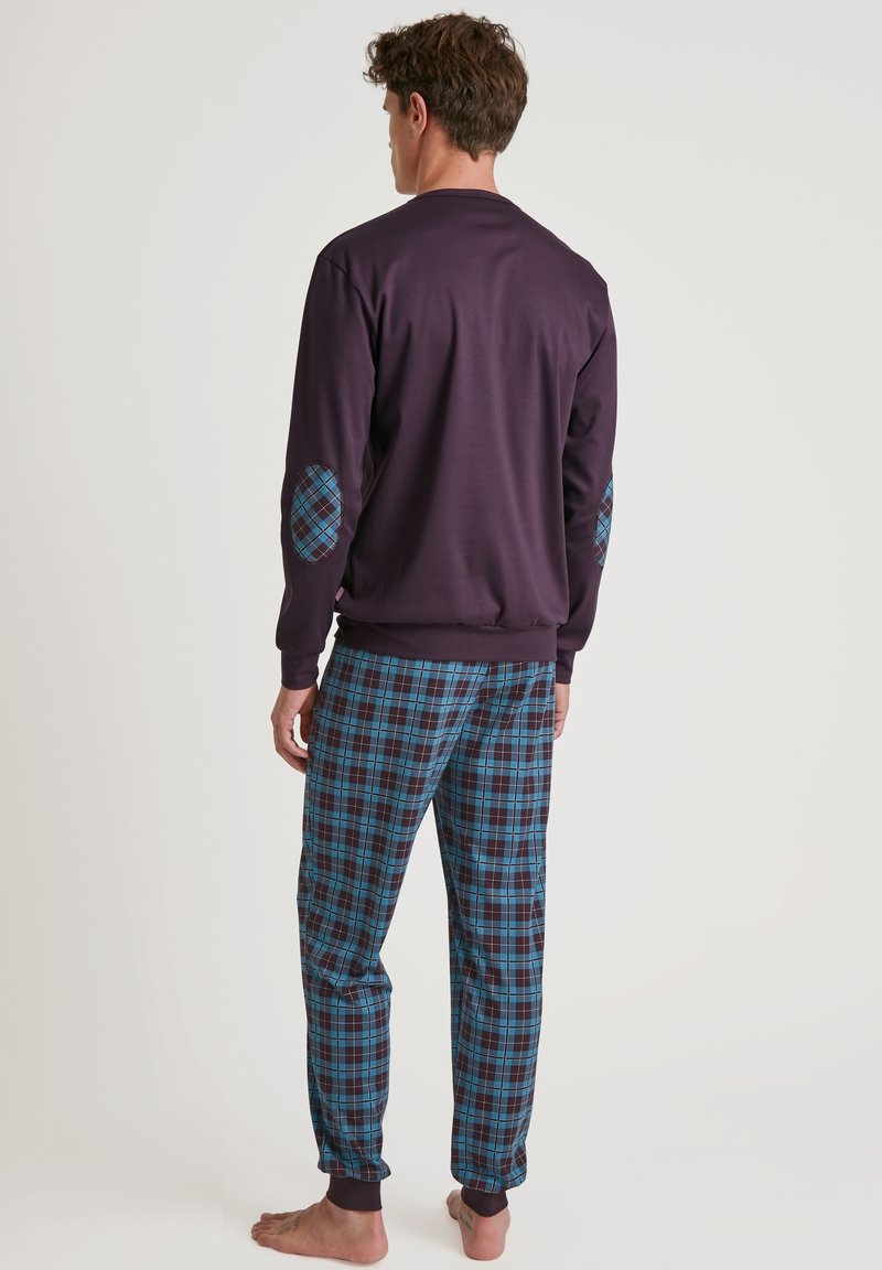 Maglione a maniche lunghe di colore viola con toppe blu a fantasia sui gomiti, abbinato a pantaloni a quadri blu e neri, con orli risvoltati e una vestibilità comoda.