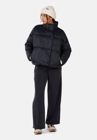 Giacca a vento nera con colletto alto e design trapuntato, abbinata a pantaloni larghi scuri e un berretto di maglia beige. Sneakers neutre.
