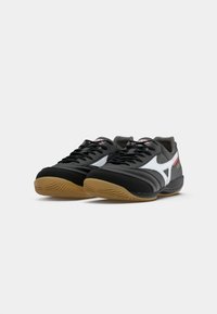 Pantofi sport negri cu accente albe, talpă din cauciuc, șireturi și guler căptușit; design curbat și suprafață texturată pentru aderență.