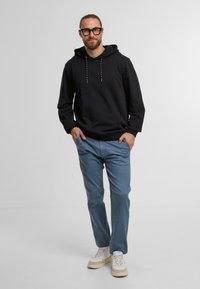 Czarna bluza z kapturem z regulowanymi sznurkami, niebieskie spodnie oraz jasne trampki. Swobodny fason z długimi rękawami i luźnym krojem.