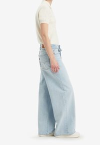 Jeans a gamba larga di colore blu chiaro, con vita alta, realizzati in denim, dotati di tasche posteriori e di una patch in cuoio marrone sulla cintura.