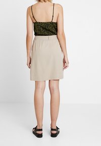 Beiger Minirock mit glatter Textur, kombiniert mit einem olivgrünen Top mit Leopardenmuster. Das Modell trägt schwarze Sandalen. Ansicht von hinten.