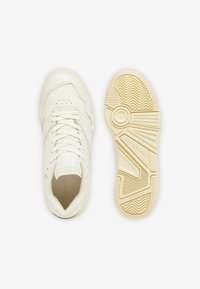 Zapatillas de cuero blancas con un upper liso, detalles perforados, cordones planos y una suela de goma texturizada en crema con un patrón geométrico.