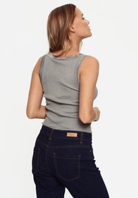 Top sin mangas de canalé gris combinado con unos jeans azul oscuro que cuentan con bolsillos traseros y una etiqueta de la marca en la cinturilla. Textura suave y diseño ajustado.