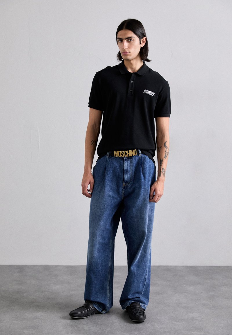 Čierna polo košeľa s logom, voľné modré rifle a čierne topánky. Zlatý opasok s dizajnom "MOSCHINO". Hladká tkanina a ležérny štýl.