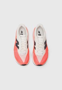 Sneakers featuring a predominantly coral upper with black accents, a white sole, and a mesh texture. Laces are white, enhancing breathability.
